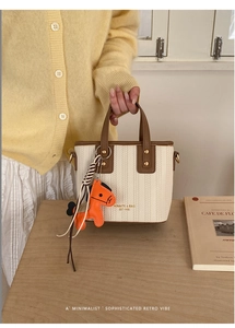 Detail of a beige woven bucket bag with brown leather trim and orange horse charm