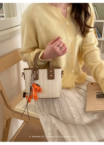 Detail of beige woven bucket bag with brown leather trim and orange horse charm accessory