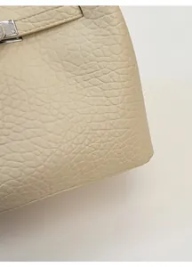 Detailed close-up of cream leather bucket bag showing silver clasp and fine pebble grain