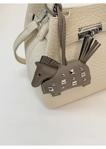 Detail of dark grey leather horse charm with silver rivets on a white handbag