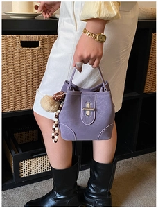 Close-up of taro purple leather bucket bag with metallic twist lock and pom-pom charm