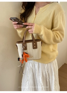 Detail of woven bucket bag with brown leather trim and orange puppy charm on a model