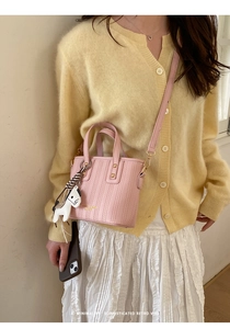 Detail of pink woven bucket bag with white horse charm and adjustable leather strap