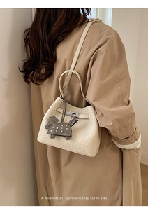 Detailed shot of cream bucket bag with lychee grain leather and pony charm on beige coat