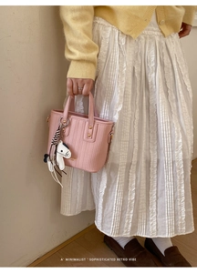 Detail of pink woven bucket bag with gold hardware and horse charm on a female model