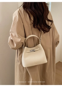 Close-up of beige bucket bag showing grainy leather texture and metal buckle on the street