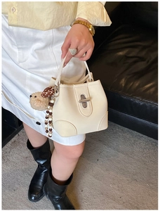 Detail of creamy white bucket bag featuring a metallic swivel lock and cute plush bear charm