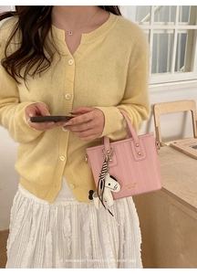Pink textured bucket bag with golden studs and a horse charm charm held by a model