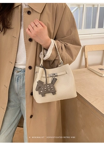 Detail of beige grained leather handbag featuring silver twist lock and horse charm decor