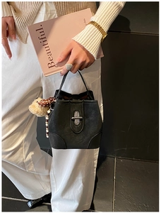 Detail of black bucket bag with silver cross lock and cute plush bear charm accessory