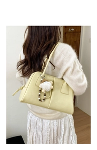 Detail of cream leather shoulder bag with plush doll charm and beaded chain on a model