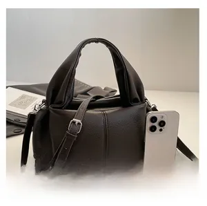 Detail shot of brown lychee grain leather handbag showing size compared to a smartphone