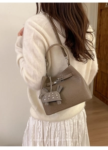 Close-up of minimalist khaki bucket bag with silver turn-lock and leather horse charm