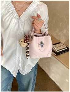 Detail of pink leather bucket bag featuring a metal buckle and cute bear charm