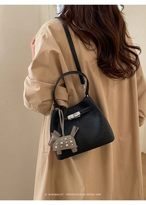 Detail of black litchi leather bucket bag with silver lock and horse charm decor