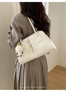 Minimalist beige leather shoulder bag featuring a bohemian tassel and pompom charm detail
