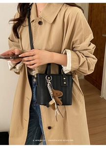 Black woven bucket bag with brown puppy charm worn with a beige trench coat