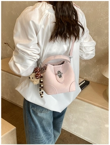 Pink leather bucket bag with bear pendant shown on model in a stylish indoor setting