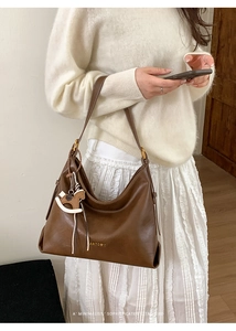 Detail of a brown leather tote bag with Antoor logo and unique rocking horse charm