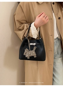 Detail of black lychee grain bucket bag with silver twist lock on khaki trench coat