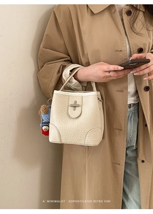 Close-up of beige lychee grain bucket bag with a cute bear charm and silver twist lock