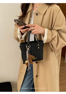 Detail of black woven bucket bag with gold rivets and leather horse charm on beige coat