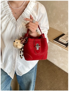 Detail of red faux suede bucket bag with silver turn-lock and plush bear charm