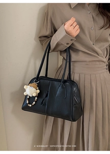 Detail of black matte leather shoulder bag with plush pendant and wooden bead decoration