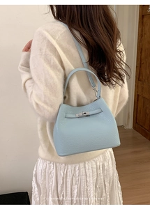 Close-up of light blue crocodile embossed handbag with silver metal buckle on model