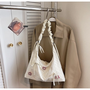 Detail of cream tote bag featuring floral accents, ribbon bows and ruched shoulder strap