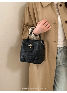 Detail of black lychee grain bucket bag with gold metal clasp on khaki trench coat