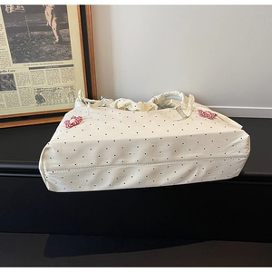 Close-up of cream canvas tote bag with black polka dots and red floral ribbon accents