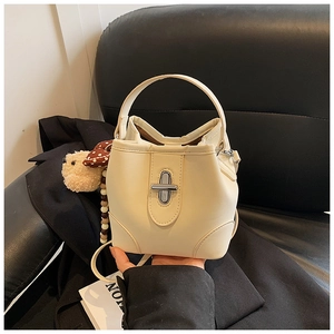Detail view of off-white bucket bag featuring silver twist lock and cute bear charm pendant