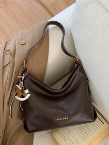 Vintage dark brown leather hobo bag with white stitching on a soft white sofa