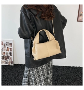 Model wearing a beige soft leather pleated dumpling bag with handle and shoulder strap