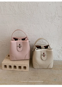 Detail of lychee textured leather bucket bags in soft pink and cream with metal clasps