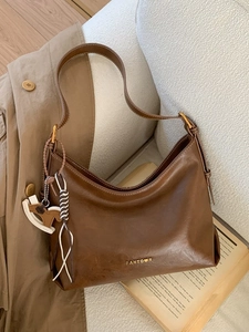 Vintage brown leather tote bag with gold logo on sofa next to a trench coat and book