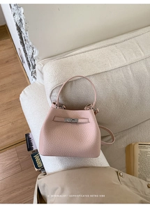 Close-up of pink litchi grain leather bucket bag with silver turn-lock on soft sofa