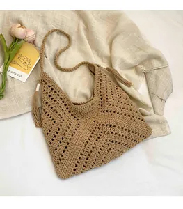 Detailed close-up of dark khaki hand-woven straw bag with fringe tassel and hollow pattern