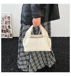Close-up of off-white lychee grain leather cloud bag held by model in casual urban setting