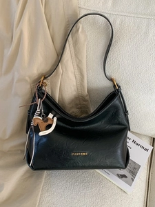 Black textured leather hobo bag with gold hardware and pony charm on white sofa