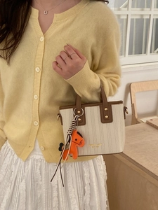 Chic textured bucket bag with brown handle and orange horse charm on a yellow cardigan