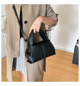 Black lychee leather cloud bag with ruched handle shown on a stylish trench coat