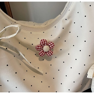 Close-up of cream floral tote bag featuring black polka dots and a red plaid fabric flower