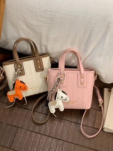 Mini lychee leather bucket tote bags in cream and pink with horse charm on wooden floor