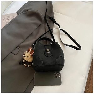 Close-up of black matte bucket bag on white bedding with a phone for size reference