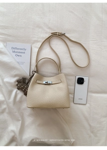 Detailed view of cream leather bucket bag with silver metal buckle and horse charm