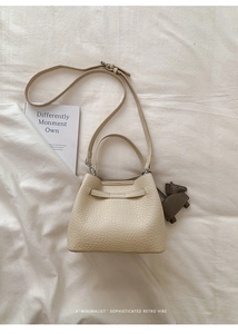 Detail of cream bucket bag with lychee texture and decorative horse leather charm
