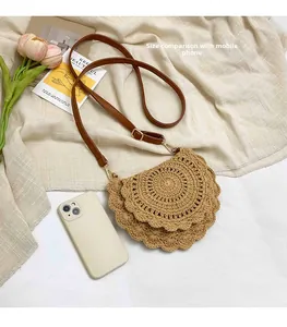 Size comparison of a semi-circular straw crossbody bag next to a mobile phone