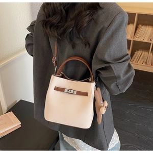 Detail of beige bucket bag with brown straps and plush charm worn with a grey blazer
